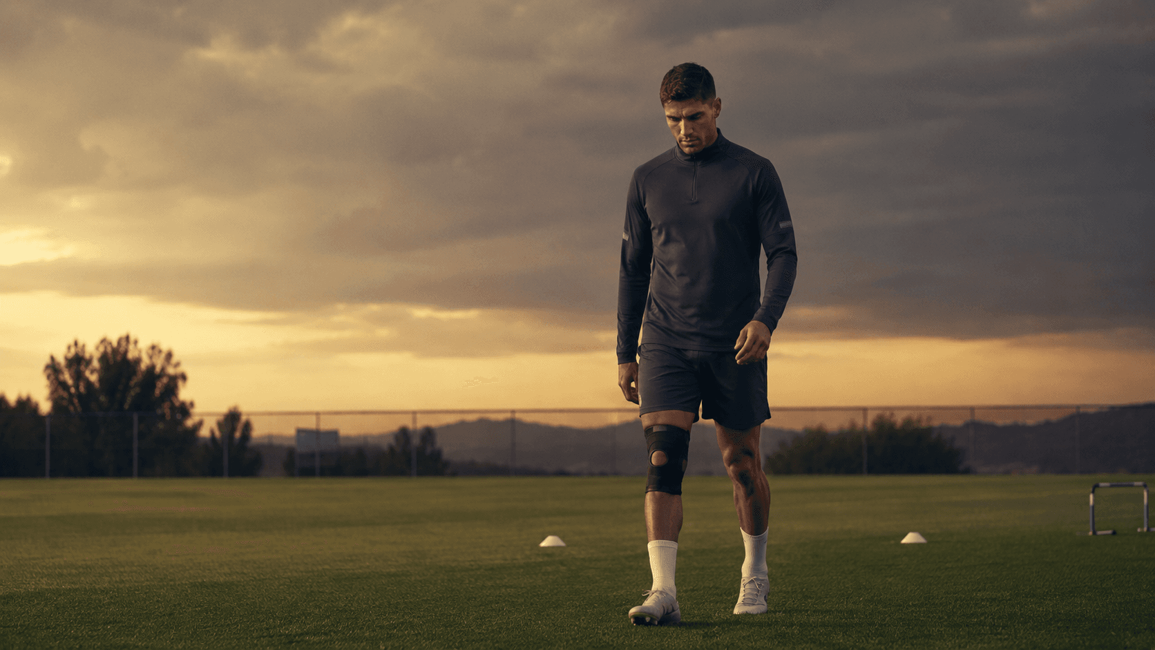 Twenty-two months — Rodri alone on a training pitch at golden hour, knee brace visible, walking back toward the game that nearly left him behind