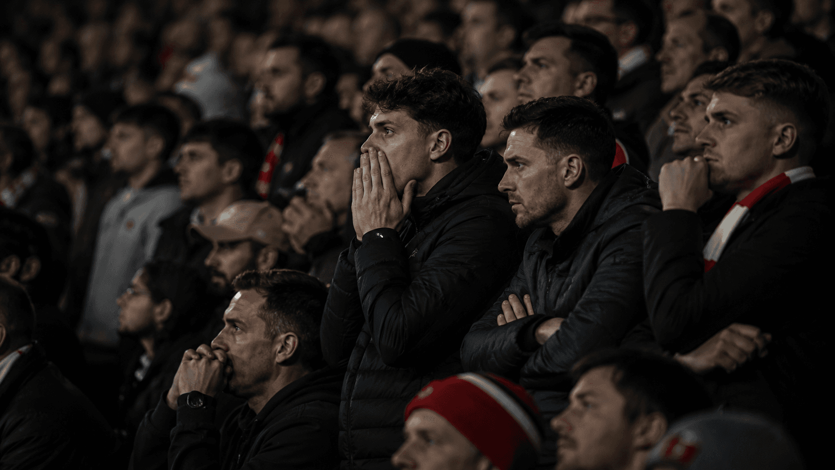 A section of the Emirates crowd frozen mid-breath, scarves raised, eyes fixed on the pitch