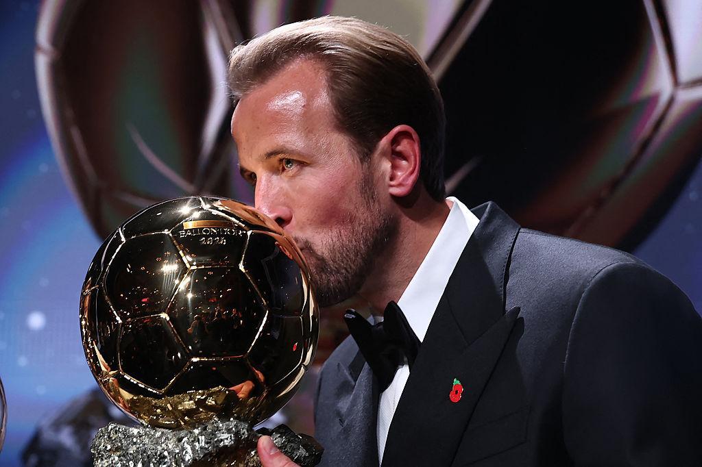 Harry Kane, in a black tuxedo with a poppy on his lapel, kisses the Ballon d'Or trophy on stage in London